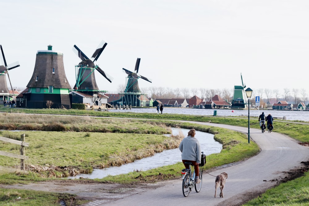 a person riding a bicycle with a dog on a path by a windmill