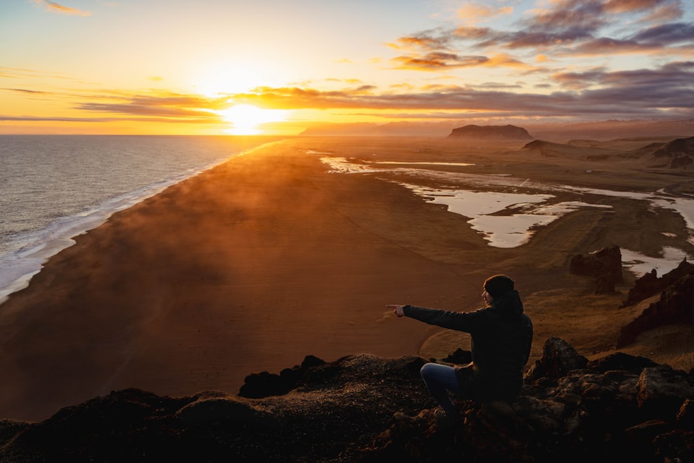 a person sitting on a rock looking at the ocean