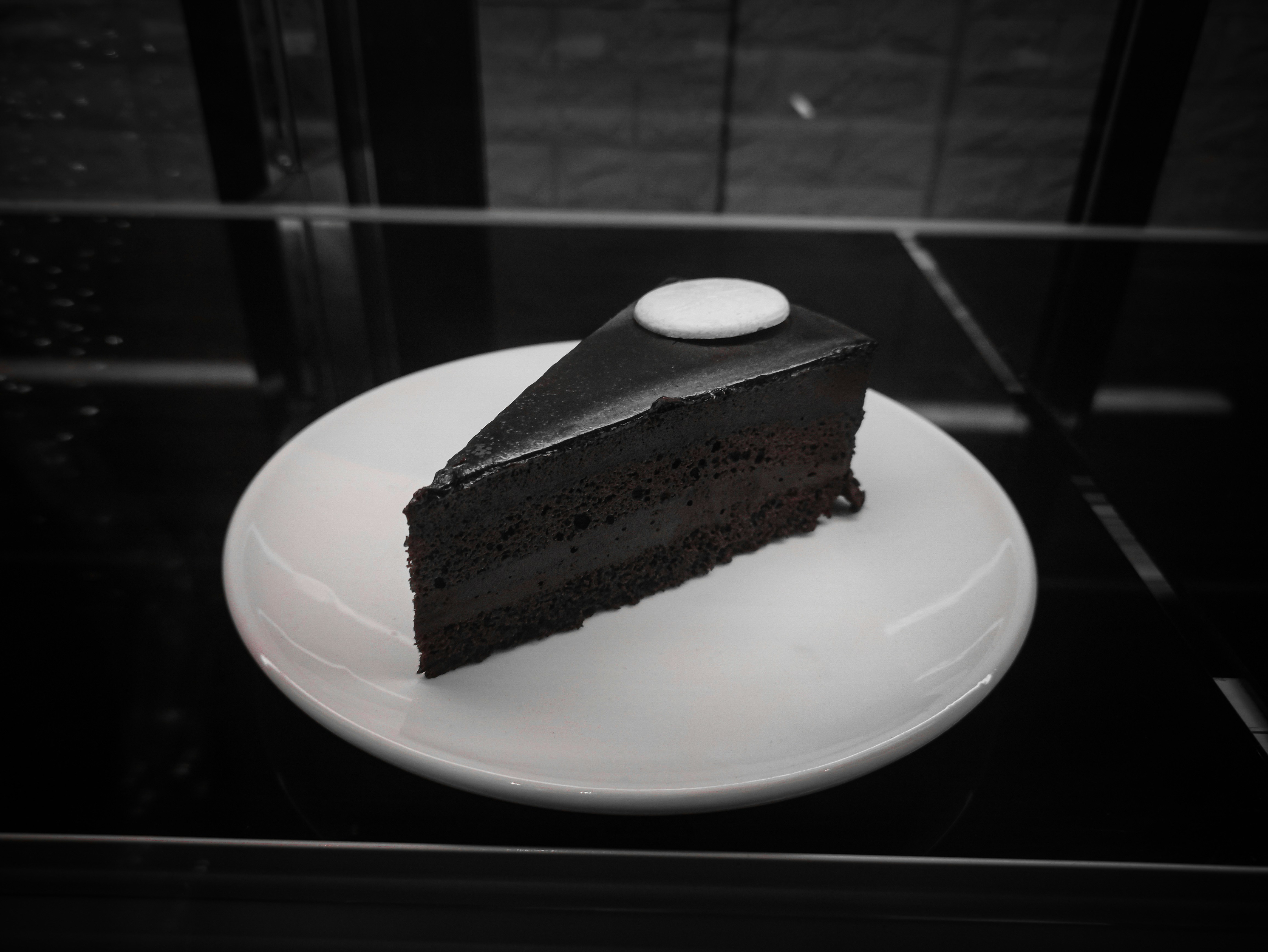 Dark chocolate soft cake slice with glossy ganache on black background, dramatic shadow lighting