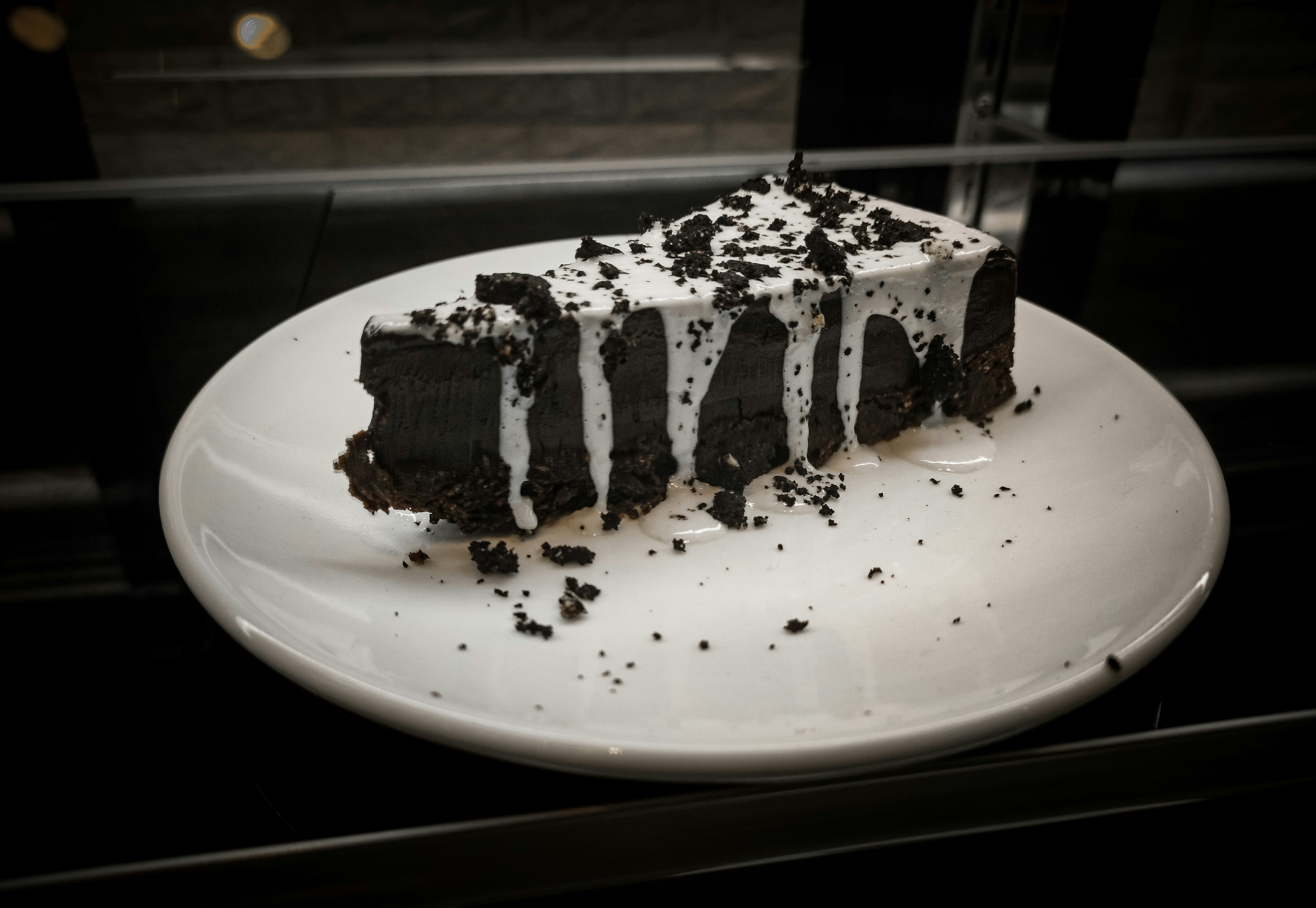 Decadent dark chocolate cake slice with glossy ganache drizzle and praline crumbs on black slate surface