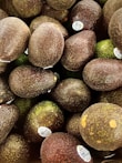 A pile of avocados with varying shades of dark green and brown, some with stickers indicating they are from Mexico.