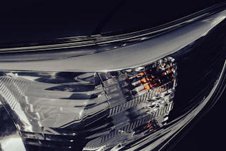 Detail of a car's headlight with soft glow and metallic reflections on a deep gray textured surface.