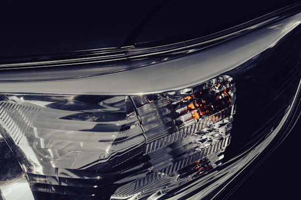 Detail of a car's headlight with soft glow and metallic reflections on a deep gray textured surface.