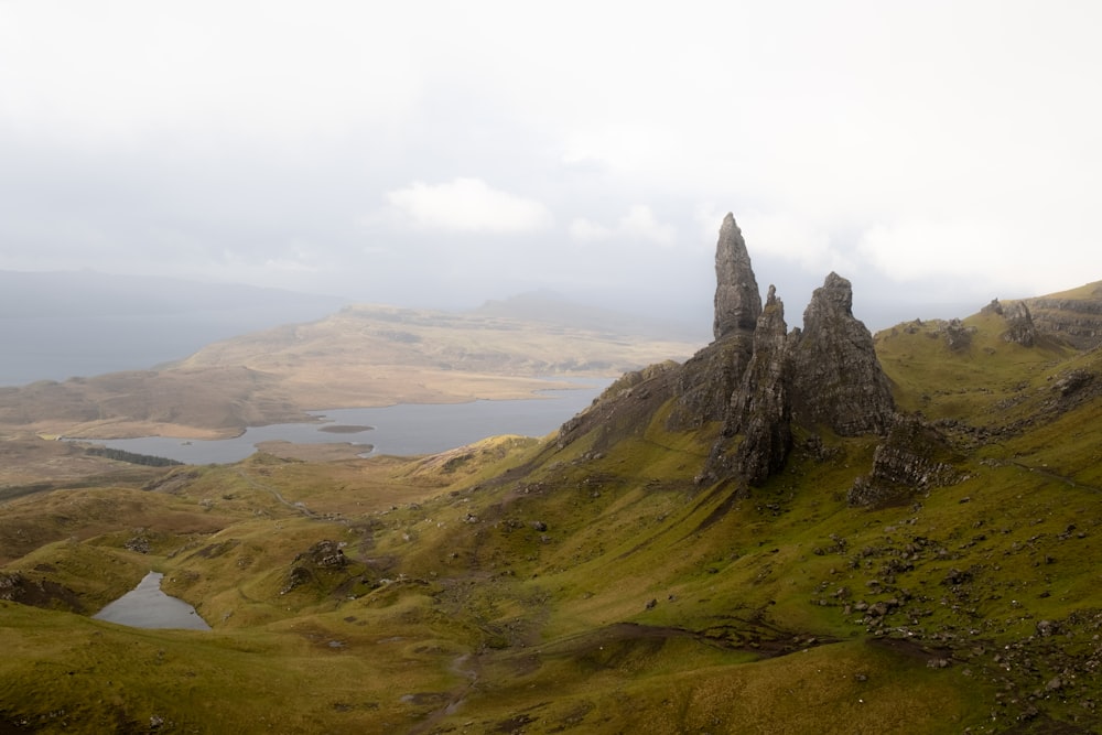 ein grasbewachsener Hügel mit einem Gewässer in der Ferne mit The Storr im Hintergrund