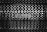 An intricate pattern of hexagonal holes forms a metal grate, likely used for fencing or as an industrial barrier. The surface appears worn and rusted, conveying a sense of age and industrial use.