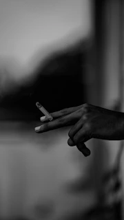 Close-up of a hand holding a lit cigarette next to a glass of liquor, capturing a moment of relaxed sophistication.