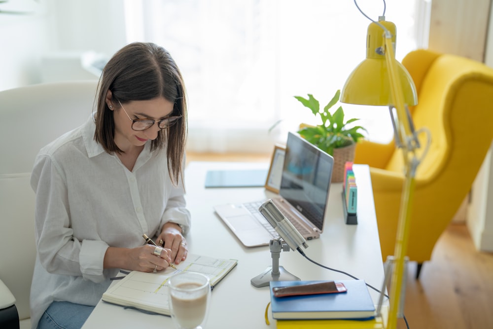 a woman sitting at a table with a laptop and a phone