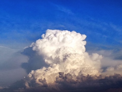 A large, billowing cumulus cloud dominates the sky, with its bright white and grey tones contrasting against a backdrop of deep blue. The cloud formation is dense, resembling a towering structure.