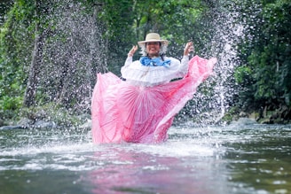 a person in a pink and white dress in a river with a pink and white fish jumping out