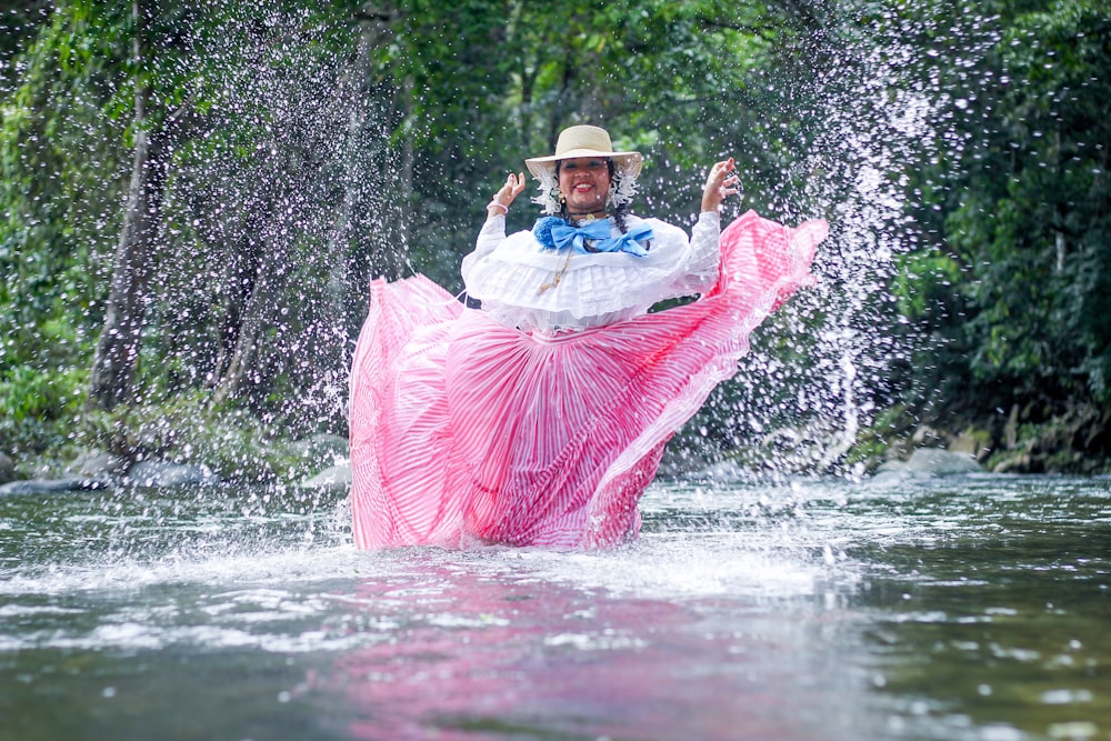 a person in a pink and white dress in a river with a pink and white fish jumping out