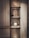 A stylish interior setup featuring a wooden shelf with multiple levels, displaying decorative items. The top shelf holds a round, ribbed vase. The middle shelf contains a black square object, a small round dish, and a striped container. Below, a spherical white vase is illuminated, creating a focal point. The backdrop has vertical metallic strips adding texture and visual interest.