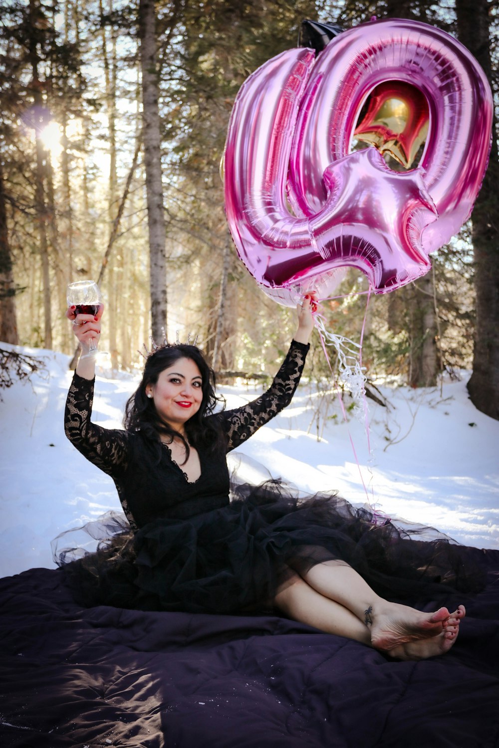 a person in a black dress holding a pink balloon in the snow