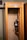 An old-fashioned telephone booth with a rotary payphone mounted on the wall. The payphone features a coin slot, a rotary dial, and a metal cord connecting the handset. The booth is made of wood, with a small shelf underneath the phone.