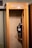 An old-fashioned telephone booth with a rotary payphone mounted on the wall. The payphone features a coin slot, a rotary dial, and a metal cord connecting the handset. The booth is made of wood, with a small shelf underneath the phone.