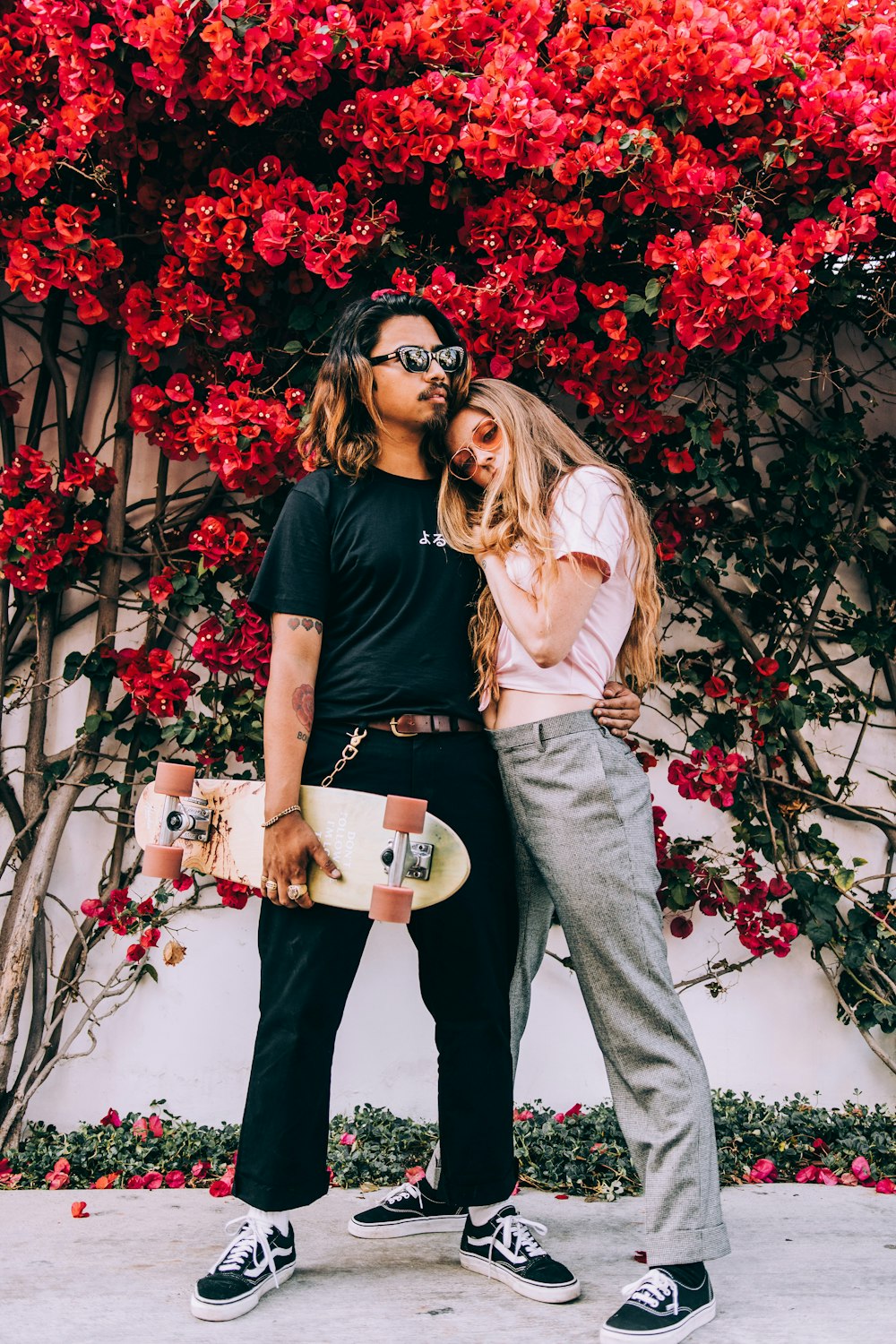 a man and woman posing in front of a tree with red flowers