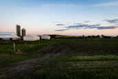 A peaceful rural landscape with barns and silos at sunset.