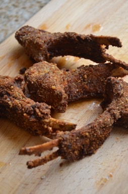 Several pieces of fried, breaded meat with visible bones are placed on a wooden cutting board. The meat appears crispy and well-seasoned.