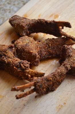Several pieces of fried, breaded meat with visible bones are placed on a wooden cutting board. The meat appears crispy and well-seasoned.