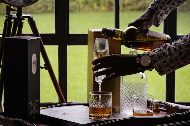 Chef Greg laughing while pouring Scotch into a tasting glass with a backdrop of Scottish hills