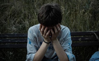 a person sitting on a bench with their hands on their face