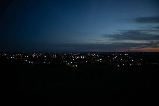 A serene nighttime cityscape bathed in deep blue with subtle gold lights glowing softly.
