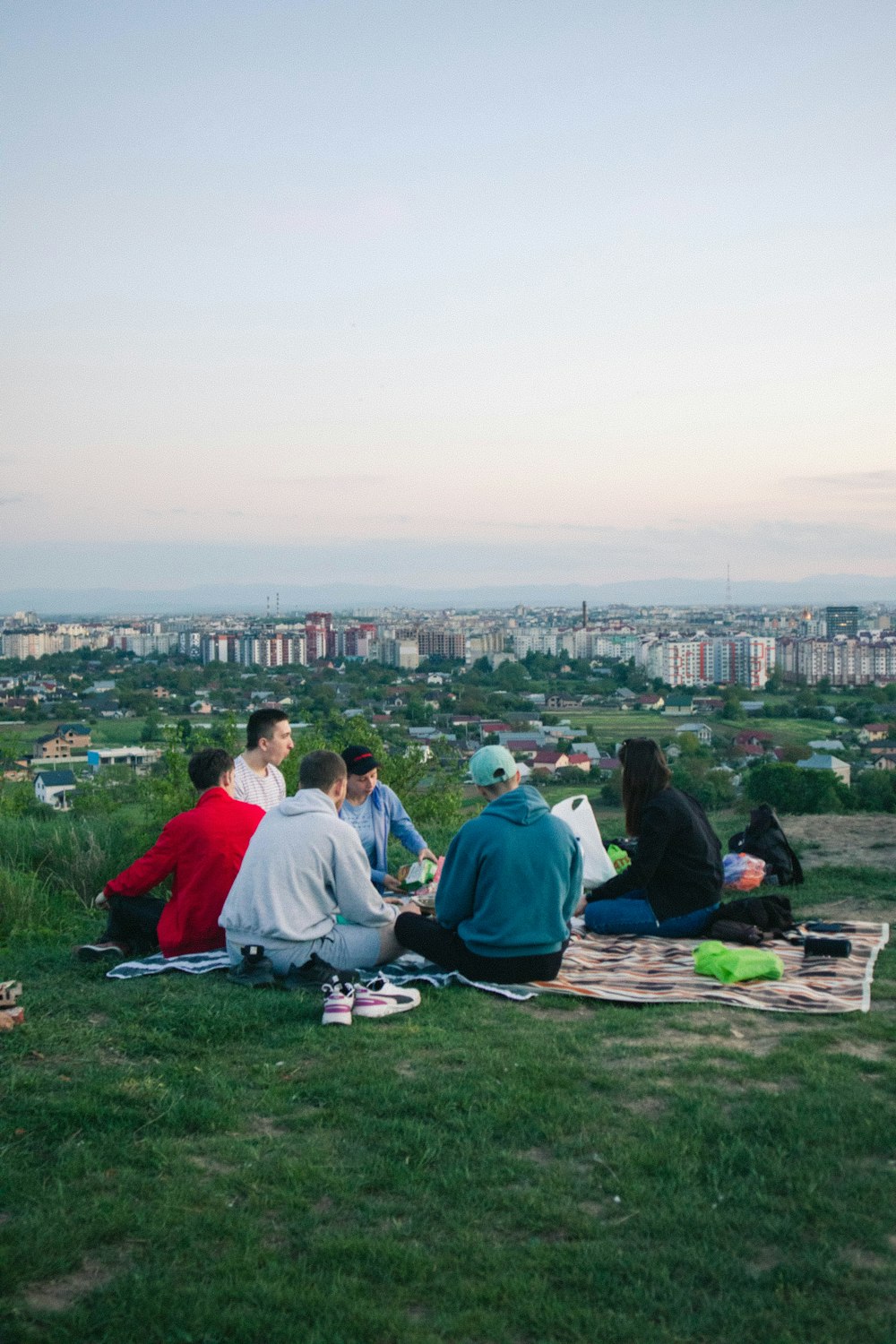 a group of people sitting on a grassy hill overlooking a city