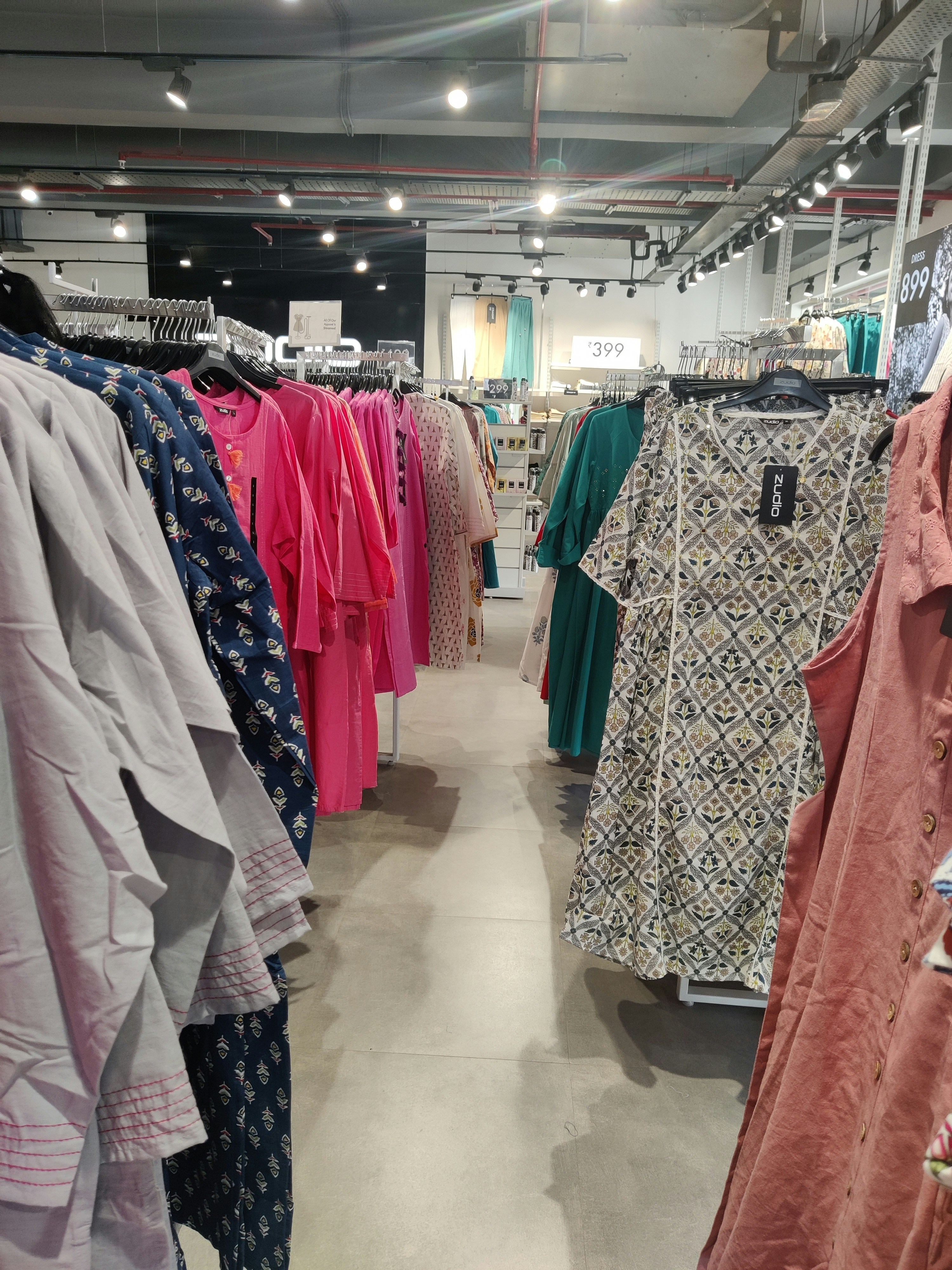 Colourful assorted secondhand clothing hanging on racks in bright market — diverse garments, vibrant colours, well-lit retail space