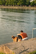 a person and a dog sitting on a rock by a body of water