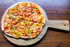 A colorful pizza topped with melted cheese, peppers, and olives served on a ceramic plate