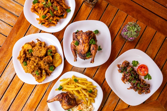 A rustic wooden table with a plate of Hatay-style chicken döner, crispy fries, a refreshing drink, and a pudding dessert, all warmly lit.