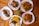 Several plates of food are arranged on a wooden table, featuring roasted chicken, fried potatoes, sautéed plantains, grilled chicken skewers, and sauced fries. Garnishes of parsley add a touch of green, with a small potted plant in the center.