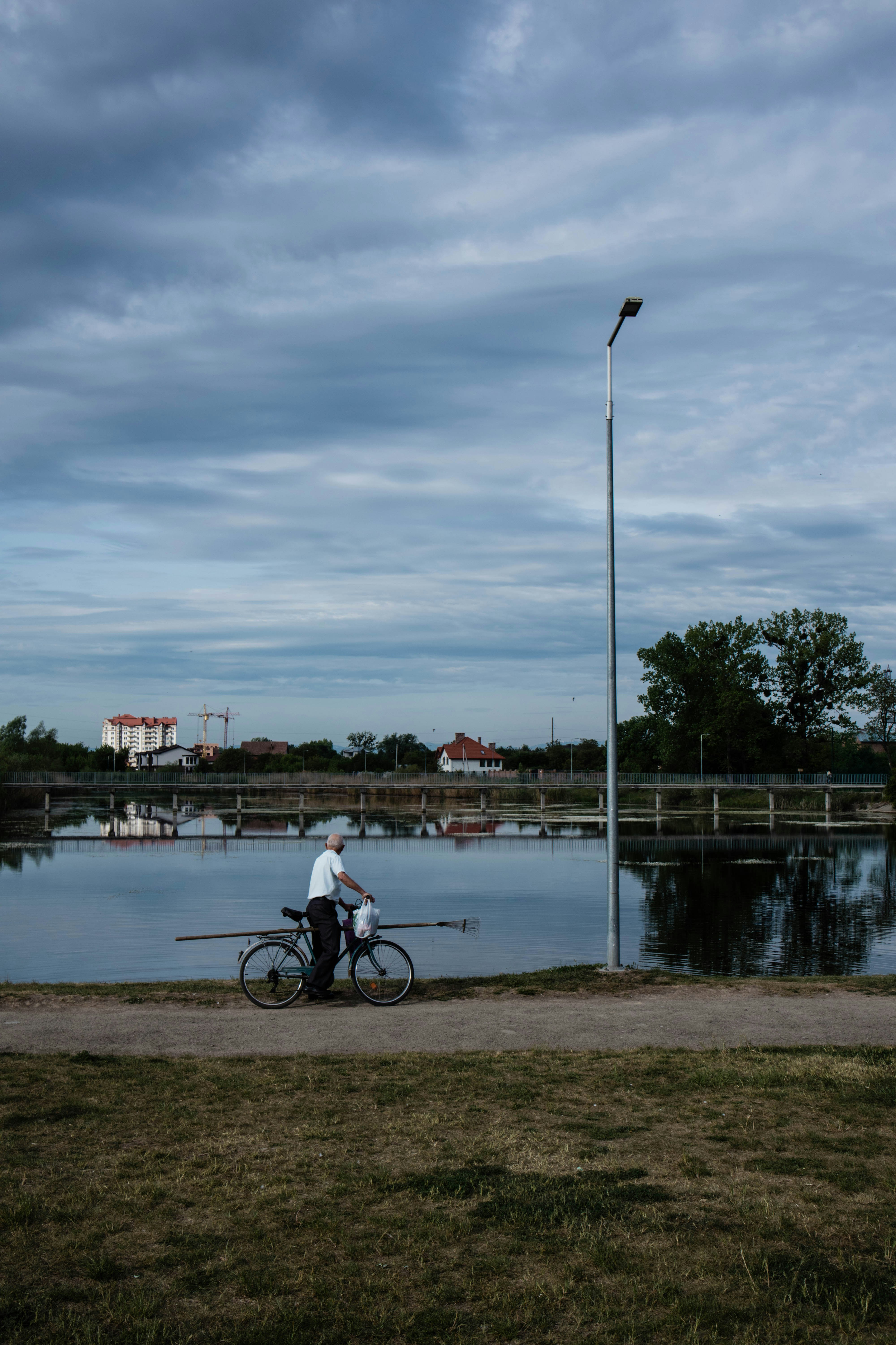 a person on a bicycle by a river with a bridge and buildings in the background