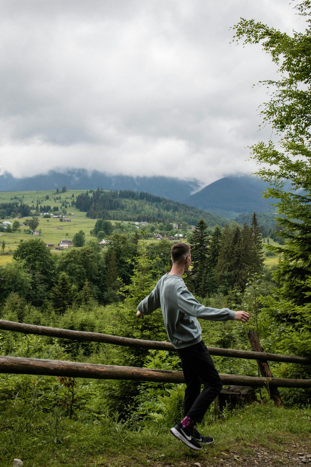 a man standing on a wooden fence overlooking a forest