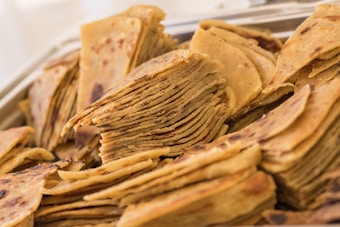 A stack of crispy, thin flatbreads with a golden-brown color, showcasing a layered texture. The bread appears freshly cooked with slight charring on some edges, suggesting a homemade or rustic preparation style.