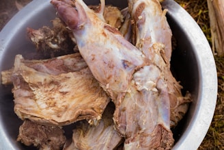 Several large pieces of cooked meat are placed in a metal bowl. The meat appears tender and slightly browned, with some bones visible. The texture suggests it has been boiled or stewed.