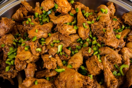 A large serving of richly seasoned and browned chicken pieces is mixed with chopped green bell peppers. The chicken appears to be cooked with spices, giving it a deep, appetizing color and a hint of oiliness.