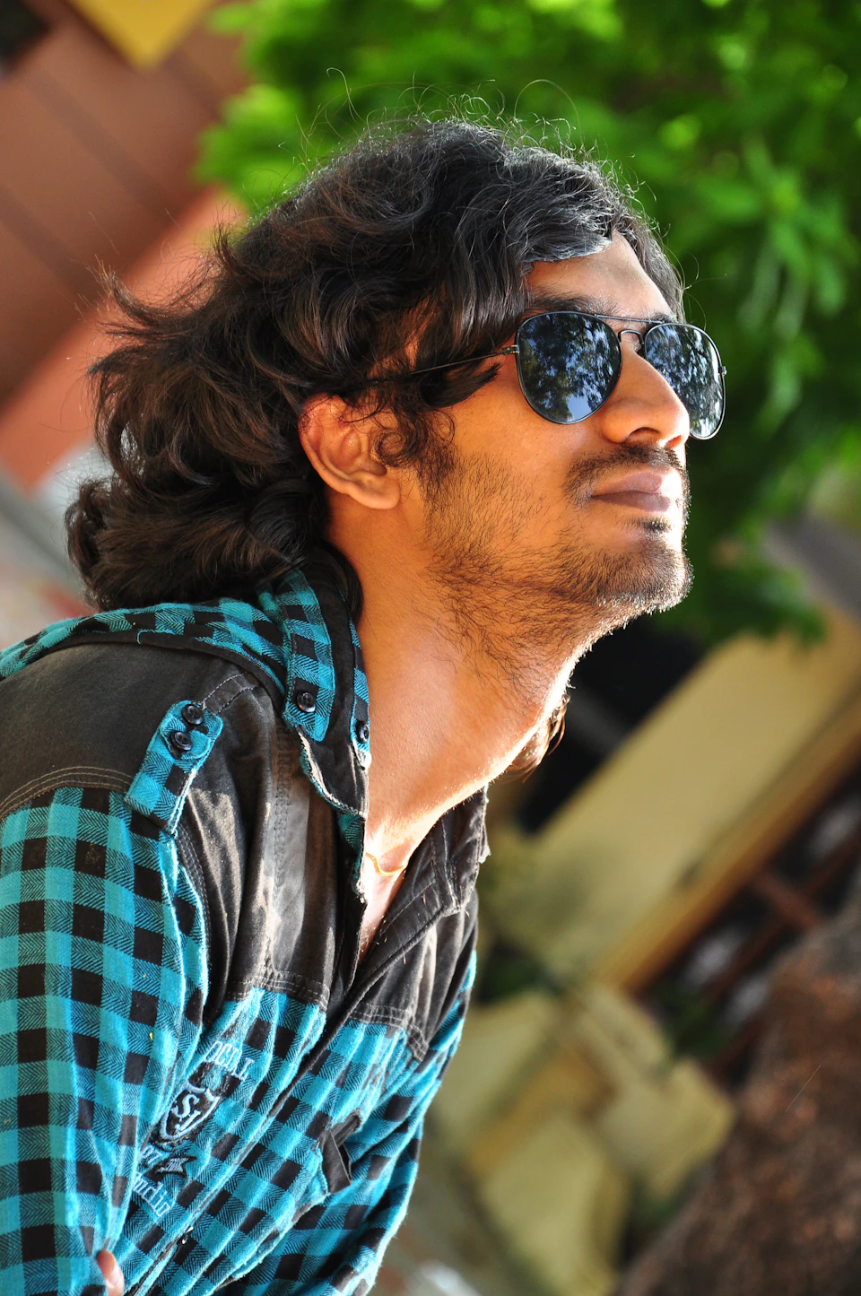 Man with long, dark hair looks off to the side while wearing sunglasses outdoors