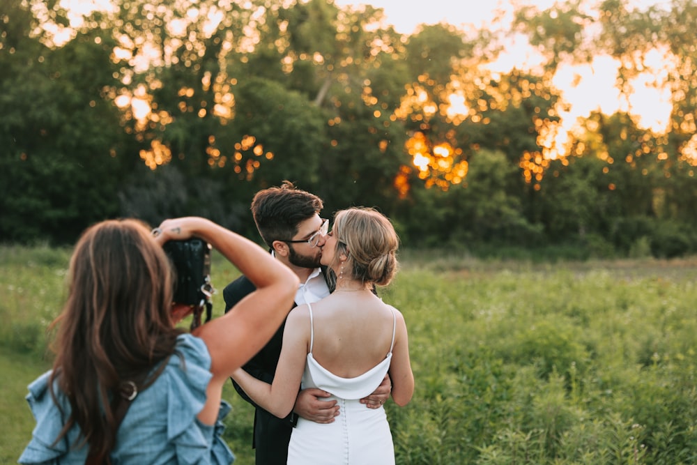 a group of people kissing in a grassy area with trees in the background