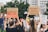 A group of people are gathered outdoors in a protest. Several individuals are holding up signs with messages, such as 'Girls just want to have fundamental rights' and 'Vasectomies prevent abortion.' In the background, more protest signs and a mix of trees and a building are visible.