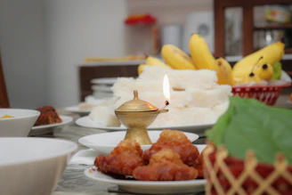 A vibrant banana leaf spread laid out on a rustic wooden table, with brass vessels and traditional kolam patterns in the background.