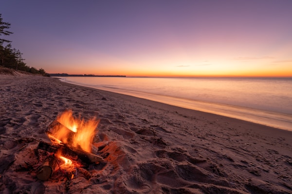 A fire on a beach with thick smoke rising into the sky