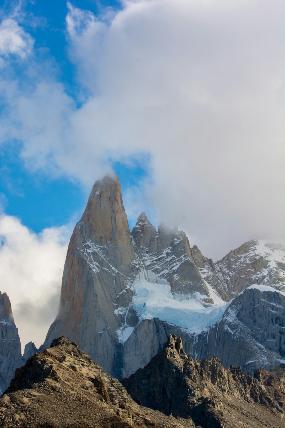 a snowy mountain with clouds with Fitz Roy in the background
