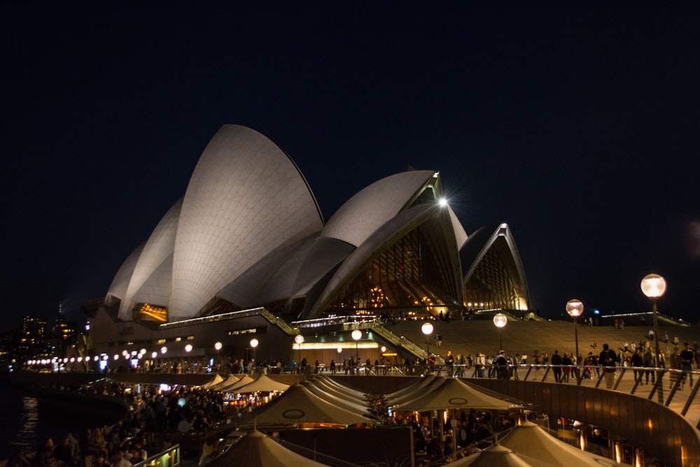 un grande edificio con una folla di persone di fronte con la Sydney Opera House sullo sfondo