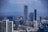 A cityscape featuring tall modern buildings and skyscrapers, with a prominent building in the center displaying the letters 'NBO'. There is a highway running through the scene, leading towards a distant, hazy mountainous horizon. The sky is partly cloudy.
