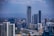 A cityscape featuring tall modern buildings and skyscrapers, with a prominent building in the center displaying the letters 'NBO'. There is a highway running through the scene, leading towards a distant, hazy mountainous horizon. The sky is partly cloudy.