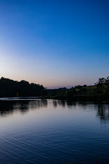 A tranquil lake reflecting the dark sky and surrounding forest, with natural blue hues blending into the minimalist scene.