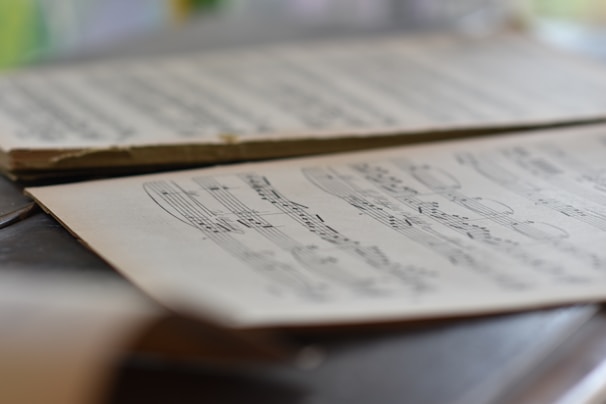 A close-up view of sheet music resting on a surface, with musical notes and symbols clearly visible. The background is softly blurred, drawing attention to the details of the musical notation.