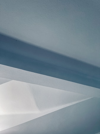 The image features an abstract composition of geometric shapes and lines, primarily in shades of blue and white. Soft lighting creates a serene and modern atmosphere, with the angles and edges adding an architectural feel.
