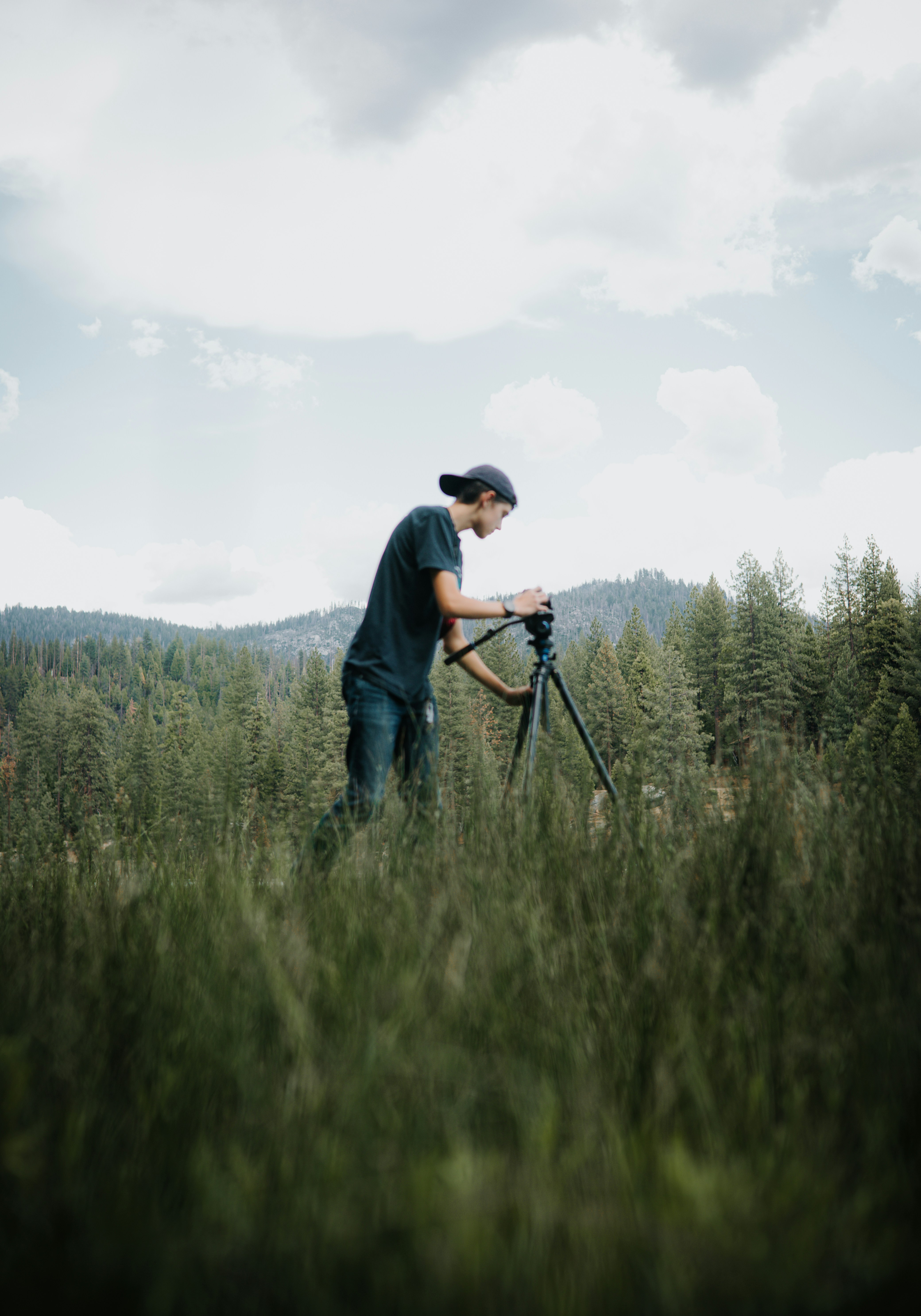 a man standing on a tripod in a grassy area with trees in the background