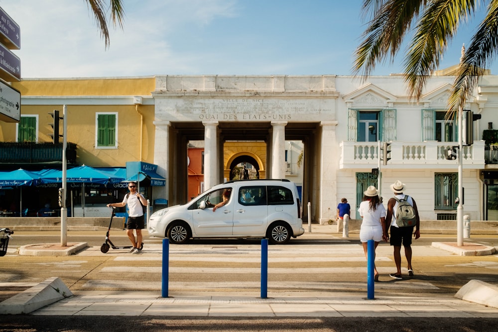 a group of people walking on the sidewalk next to a white building